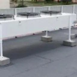 Biała, przemysłowa jednostka klimatyzacyjna z trzema wentylatorami na dachu budynku, zamontowana na betonowych podstawach.