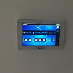 Panel sterowania alarmem domowym Satel Integra 64, wyświetlający aktualną godzinę 16:55 i datę 09/05/2019, zainstalowany na białej ścianie.