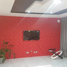 Salon z czerwoną ścianą wykończoną panelami tapicerowanymi w romby, telewizorem, rośliną doniczkową i designerskim stolikiem kawowym.