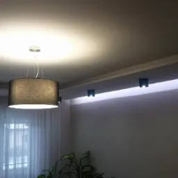 Nowoczesne oświetlenie sufitowe: wisząca lampa z abażurem i listwa z punktowymi reflektorami LED, subtelne światło w minimalistycznym wnętrzu.