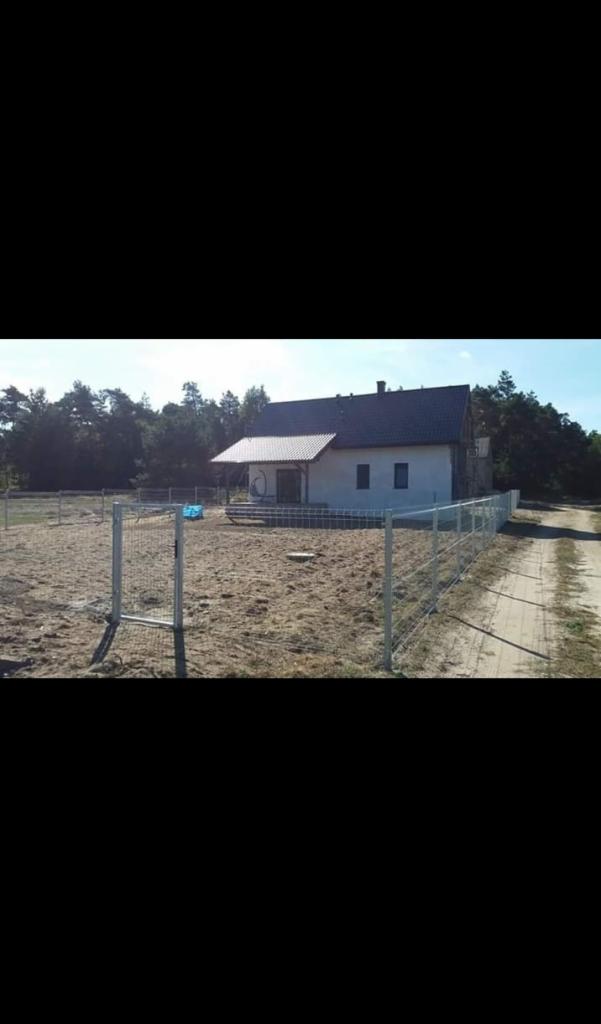 Działka z nowo postawionym ogrodzeniem panelowym wokół domu jednorodzinnego, widok z zewnątrz na niezagospodarowany teren.