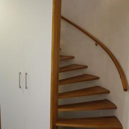 Usługi Stolarskie Andrzej Prabucki - Biała szafa w zabudowie obok drewnianych, kręconych schodów z poręczą, oświetlonych punktowym światłem.