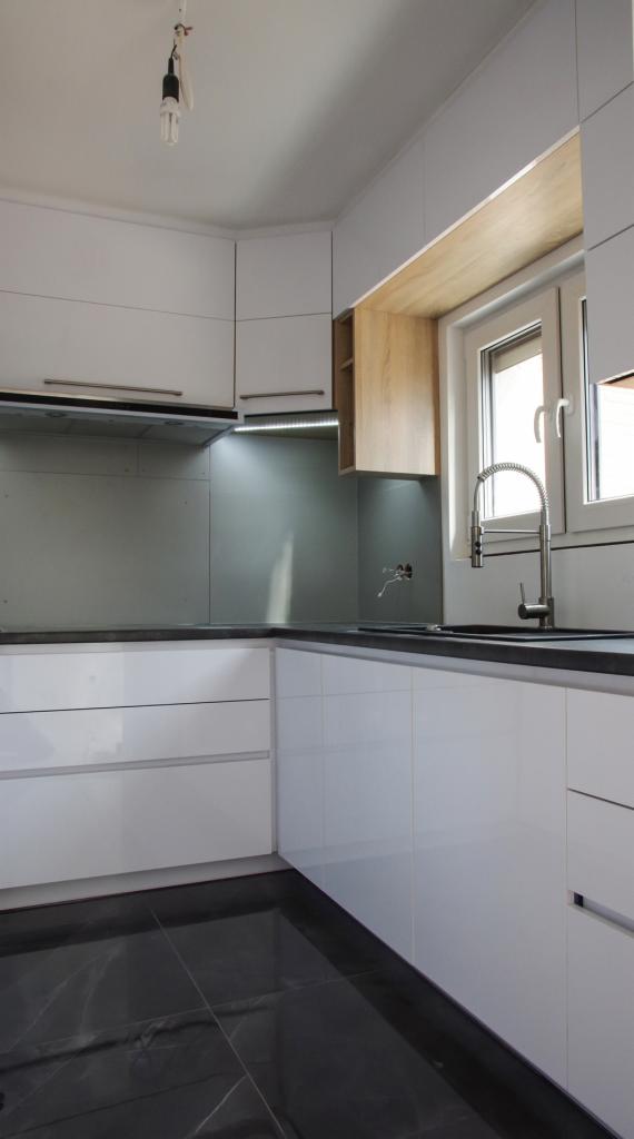 Nowoczesna kuchnia z białymi, lakierowanymi frontami szafek, czarnym blatem i błyszczącą, marmurową podłogą; widoczne niedokończone podłączenie elektryczne.