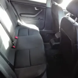 Wnętrze samochodu z widoczną tylną kanapą i fotelami przednimi, po czyszczeniu, z widocznymi pasami bezpieczeństwa i elementami tapicerki w odcieniach szarości i czerni.