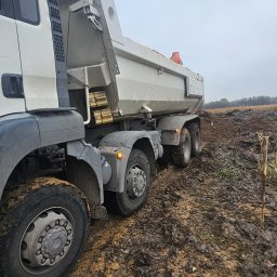 firma usługowa - Ciężarówka wywrotka na grząskim, błotnistym terenie budowy, widoczne świeżo wykopane zagłębienie w ziemi i fragment horyzontu.
