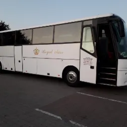 Biały autokar 'Royal Class' z otwartymi drzwiami, zaparkowany na kostce brukowej; widoczny numer telefonu firmy.