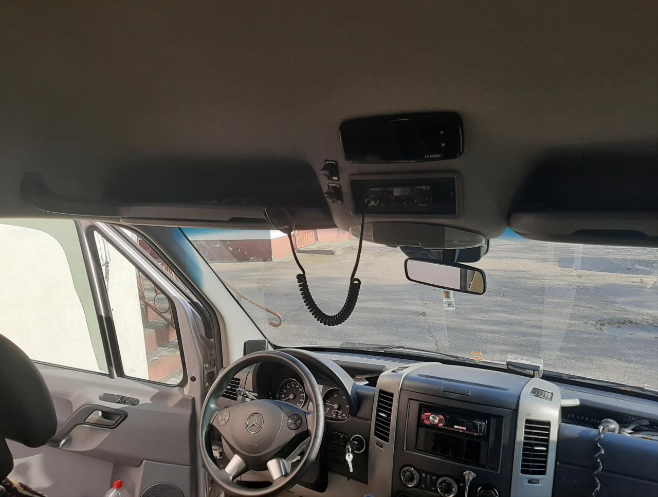 Wnętrze srebrnego busa Mercedes Sprinter z widocznym radiem CB i spiralnym kablem mikrofonu, wnętrze kabiny z czarną kierownicą z logo Mercedesa.