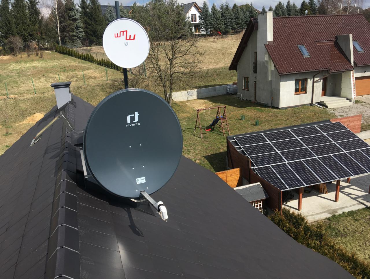 Dwie anteny satelitarne (Inverto i inna z czerwonym logo) zamontowane na czarnym dachu domu jednorodzinnego, w tle widoczny dom, panele słoneczne i huśtawka.