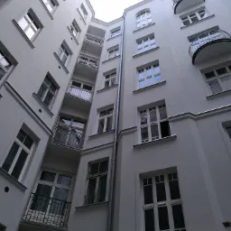 Wewnętrzny dziedziniec kamienicy po remoncie elewacji, widoczne rusztowania, odnowiona biała fasada z balkonami i oknami.