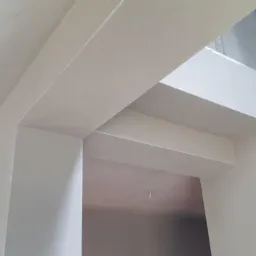 Świeżo otynkowane maszynowo nadproże i ściany w surowym stanie, widoczne fragmenty instalacji elektrycznej w tle.