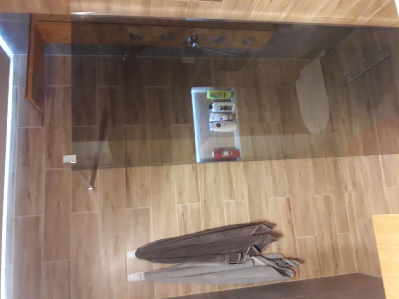 Nowoczesna kabina prysznicowa walk-in z drewnopodobnymi płytkami, szklaną ścianką i półką z kosmetykami w tle, widok z góry.