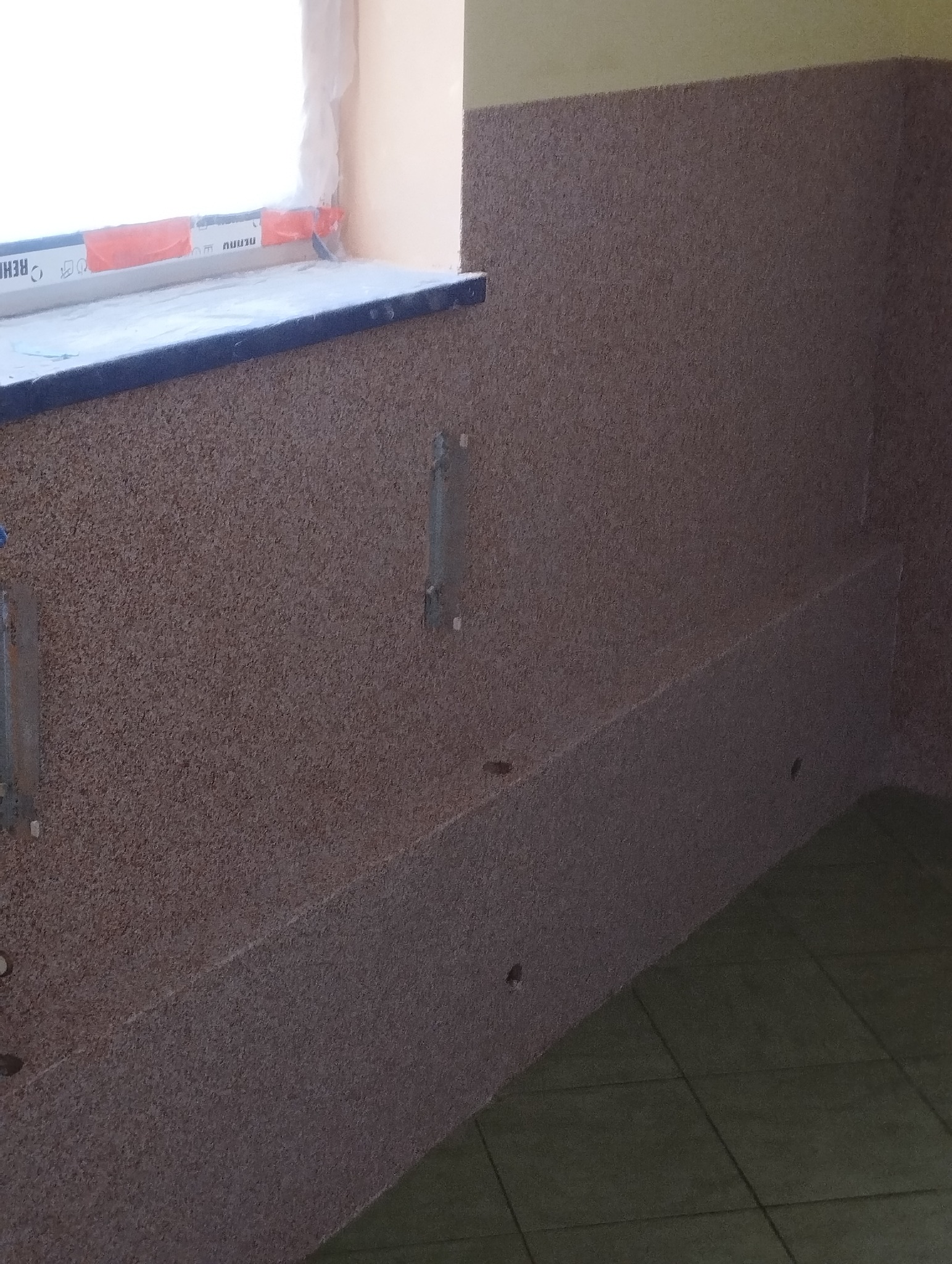 Wykończona ściana z płyt OSB w pomieszczeniu, widoczne mocowania i fragment okna. Tekstura płyty OSB dominuje w kadrze, tworząc surowy, industrialny wygląd.