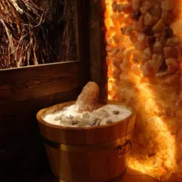 Wnętrze z drewnianym wiadrem wypełnionym solą i kryształami, oświetlona ściana z soli himalajskiej w tle.