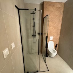 Firma ogolno budowlana Miroslaw Gros - Nowoczesna łazienka z kabiną prysznicową typu walk-in z czarnymi profilami, toaletą wiszącą i geometryczną mozaiką na ścianie. Stonowana kolorystyka.