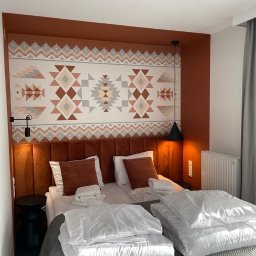 Firma ogolno budowlana Miroslaw Gros - Pokój hotelowy z łóżkiem dwuosobowym, wezgłowie w kolorze terakoty i wzorzysta tapeta w stylu etnicznym. Widoczna lampa wisząca i stolik nocny.