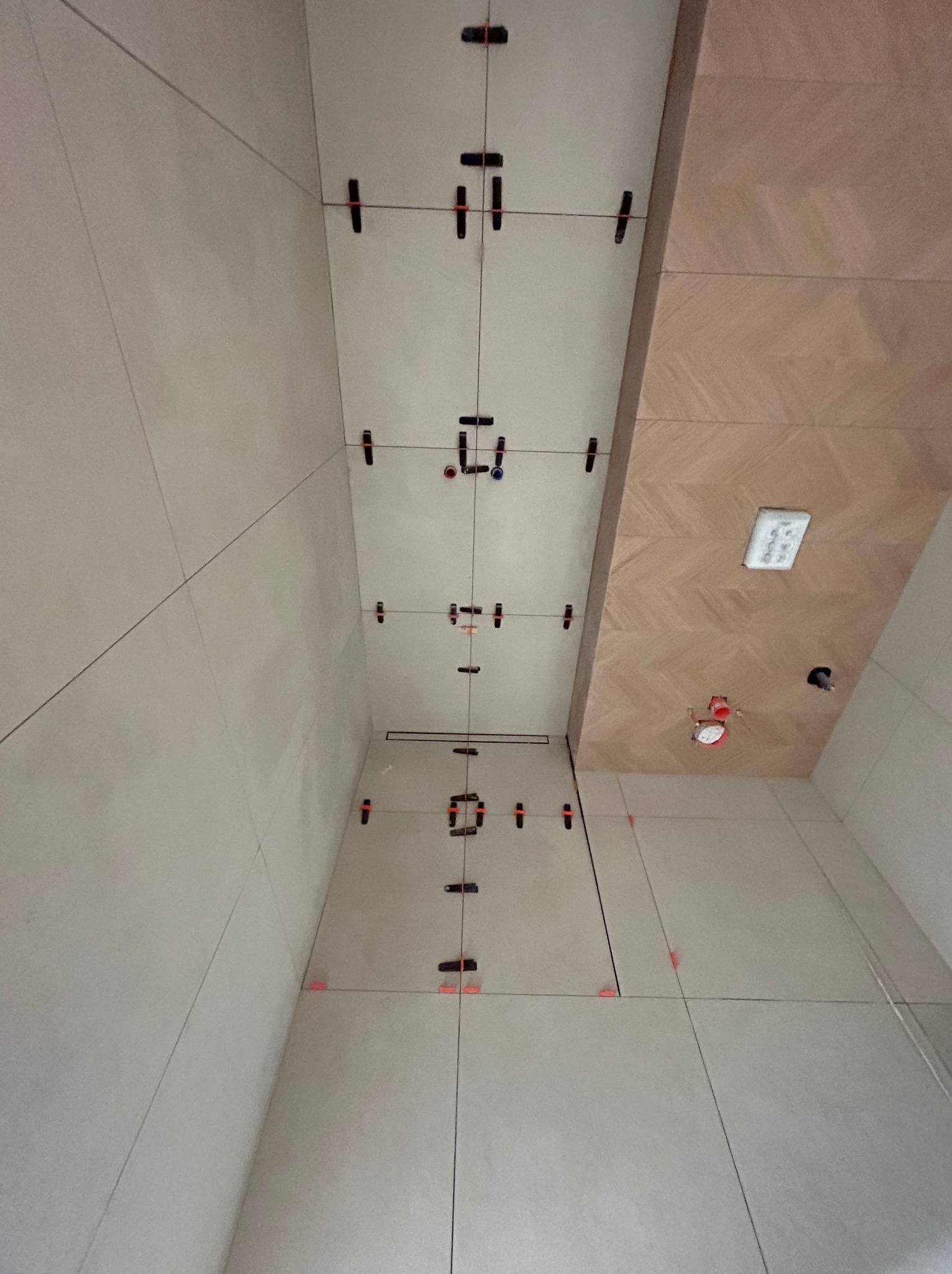 Układanie płytek w łazience z użyciem systemu poziomowania. Widoczne płytki ścienne w jasnym odcieniu, fugi oraz elementy systemu poziomowania płytek.