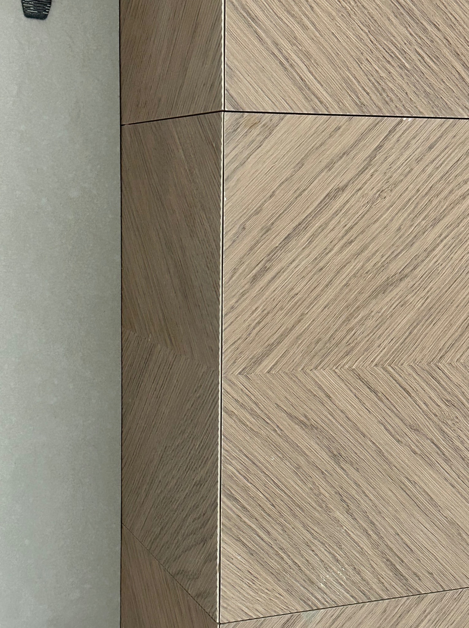 Detale wykończenia wnętrza: połączenie jasnej, matowej płytki ściennej z drewnopodobną okładziną ułożoną we wzór jodełki, z subtelnymi, złotymi akcentami w narożnikach.