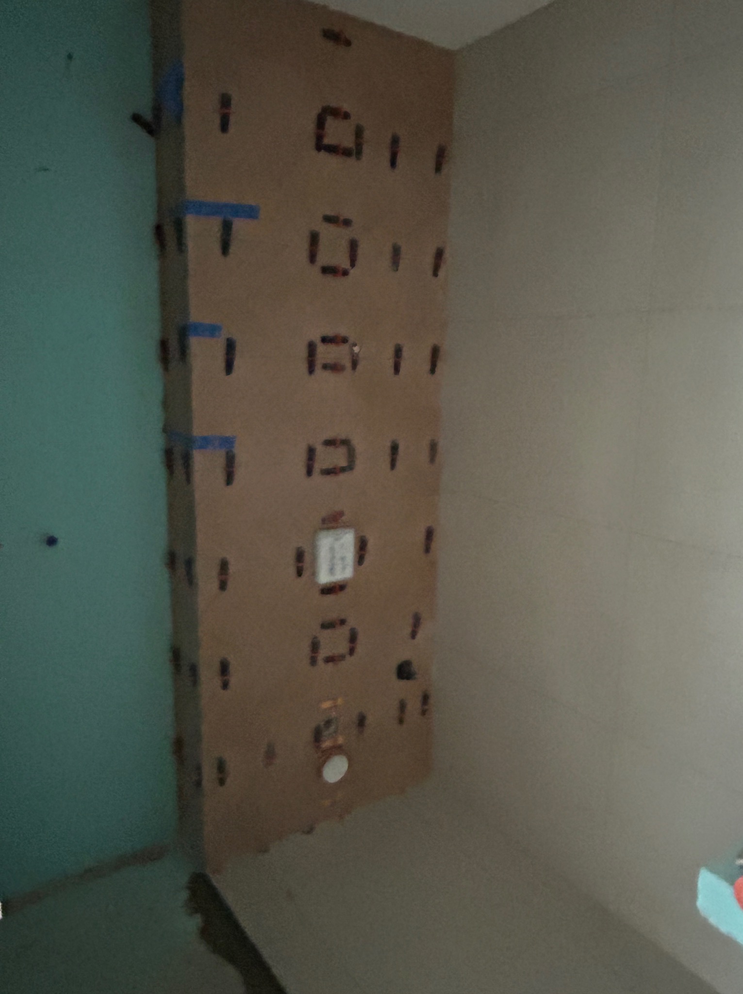 Ściana w trakcie kładzenia płytek, widoczne elementy poziomujące i pionujące, z przygotowanym miejscem na armaturę. Prace glazurnicze w łazience.