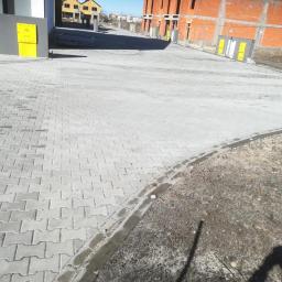 BET brukarstwo maszynowe - przemysłowe - Szara kostka brukowa ułożona na nowym osiedlu, widoczne budynki w stanie surowym i skrzynki gazowe na elewacji.