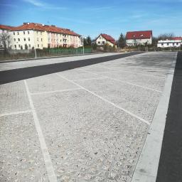 BET brukarstwo maszynowe - przemysłowe - Nowo wyłożony, pusty parking z przepuszczalnej kostki brukowej na tle budynków mieszkalnych i błękitnego nieba.