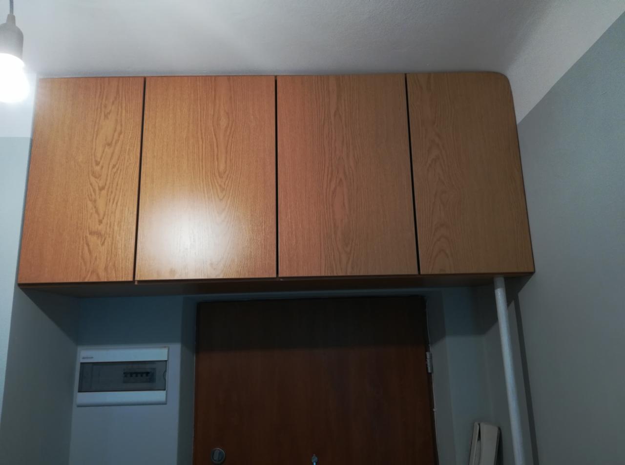 Cztery drewniane szafki wiszące nad drzwiami, z widoczną skrzynką elektryczną po lewej stronie i podporą po prawej.