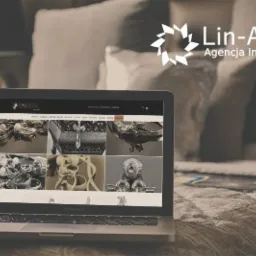Laptop MacBook Pro wyświetlający stronę internetową z galerią biżuterii, na tle poduszki i logo agencji interaktywnej Lin-Art.pl.