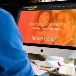 Mężczyzna w niebieskiej bluzie przegląda na iMacu stronę internetową wulkanizacji z Choroszczy, widoczne menu, logo firmy i numer telefonu kontaktowego.