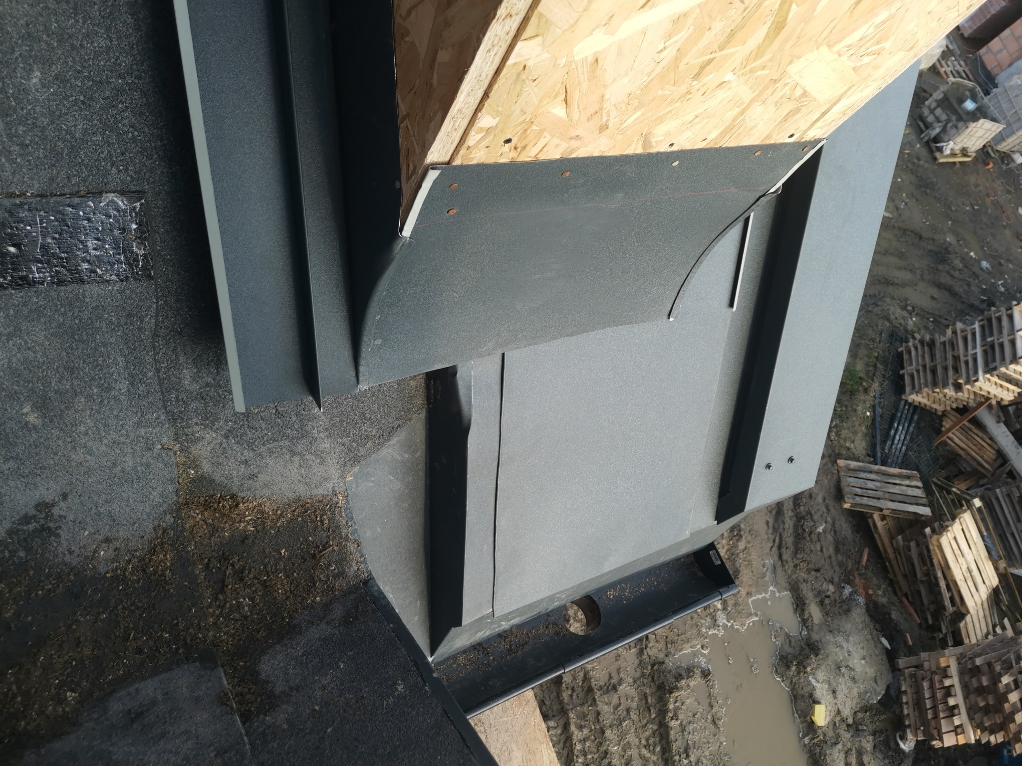 Szczegółowe ujęcie fragmentu dachu z blachy w kolorze grafitowym, ukazujące połączenie z deskowaniem i elementami odprowadzającymi wodę, widoczne ślady montażu i zabrudzenia.