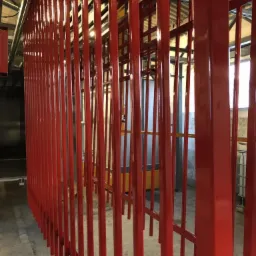 Metalowe elementy konstrukcyjne po nałożeniu czerwonej, błyszczącej powłoki ochronnej w hali produkcyjnej.