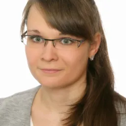 Portret kobiety w okularach, z zielonymi oczami i brązowymi włosami, uśmiechająca się delikatnie.