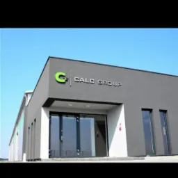 Nowoczesny budynek biurowy w szarej kolorystyce z logo Calc Group nad wejściem, błękitne niebo w tle.