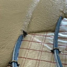 Świeżo wylana, gładka masa na ogrzewaniu podłogowym z niebieskimi rurami, widoczna siatka podkładowa z czerwonymi liniami.