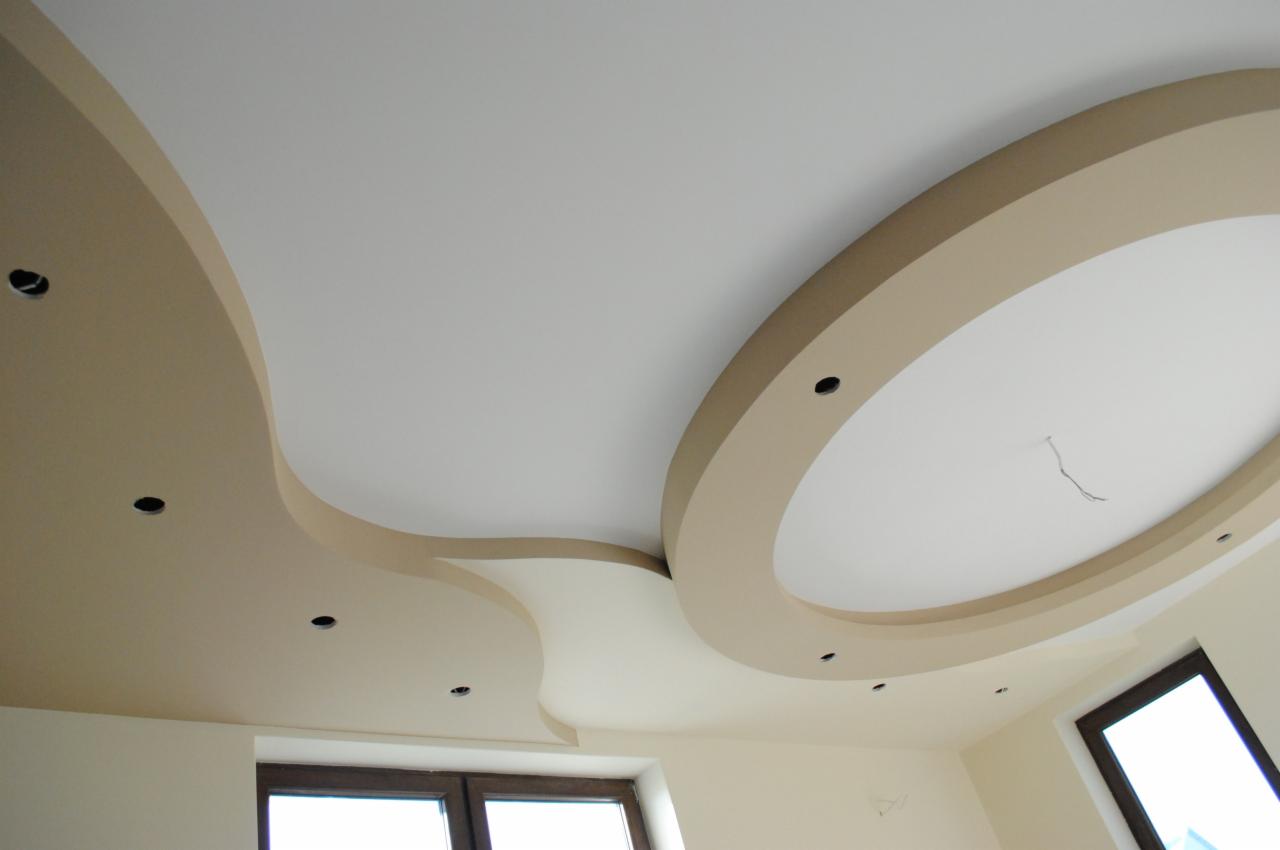 Nowoczesny sufit podwieszany z gładzią, oświetleniem punktowym i dekoracyjnymi elementami w kształcie fali i okręgu, widoczne okno.