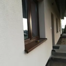 Elewacja budynku w Ligowie z oknem i narzędziami na parapecie, widoczne rusztowanie.