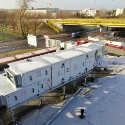 Centrala wentylacyjna z rekuperacją zamontowana na dachu budynku, widok z góry na tle miejskiego krajobrazu z wiaduktem i budynkami w oddali.