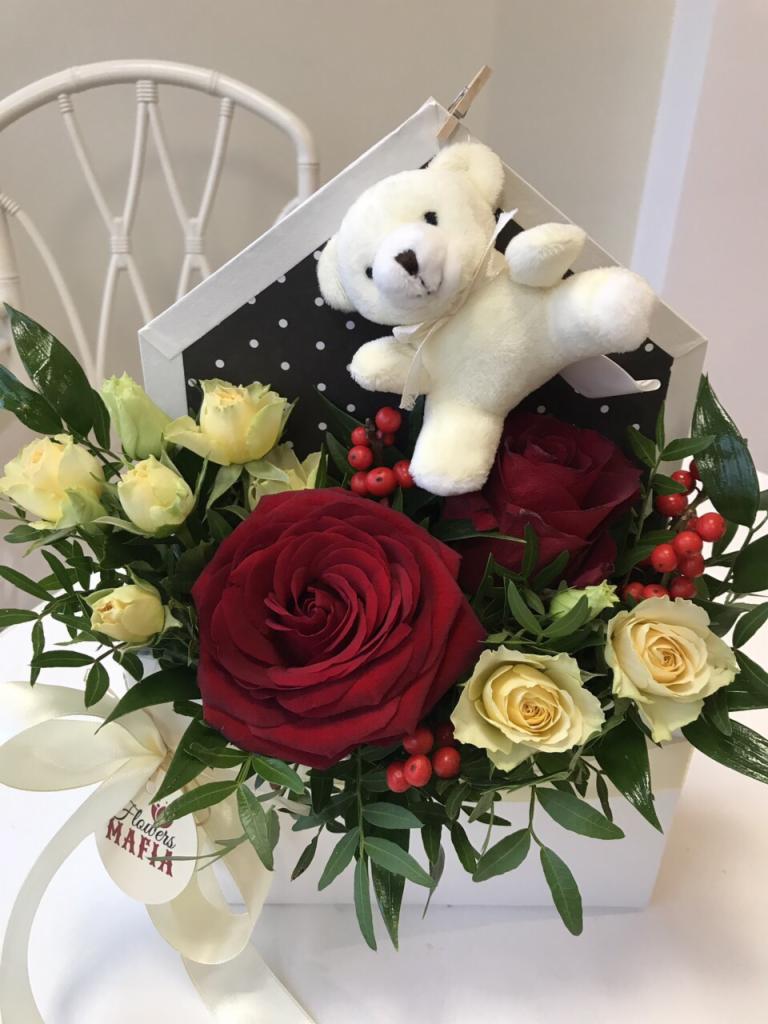 Kompozycja kwiatowa z czerwonych i kremowych róż w białym, pudełkowym wazonie z czarnym, kropkowanym tłem, ozdobiona pluszowym białym misiem z kokardą i etykietą 'Flowers Mafia'.