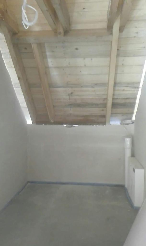 Surowe drewno więźby dachowej widoczne od wewnątrz, surowe ściany i podłoga, widoczne rury i instalacje.