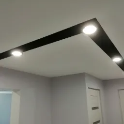 Nowoczesne oświetlenie sufitowe z czarnymi listwami i punktowymi lampami LED w świeżo pomalowanym na szaro pomieszczeniu z widocznymi drzwiami i ościeżnicą.