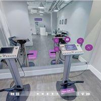 Dwa urządzenia do ćwiczeń z ekranami dotykowymi na tle lustra w jasnym, nowoczesnym pomieszczeniu treningowym z fioletowymi akcentami.