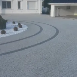 Półkolisty podjazd z jasnoszarej kostki z ciemniejszymi pasami, otoczony białym żwirem i niskimi krzewami, prowadzący do białego domu z garażem.