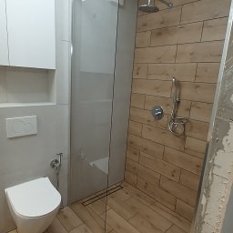 Wykończenia Wnętrz Pablo Styl Paweł Tajl - Nowoczesna łazienka z kabiną prysznicową typu walk-in, wykończona płytkami imitującymi drewno, z podtynkową armaturą i wiszącą miską WC.