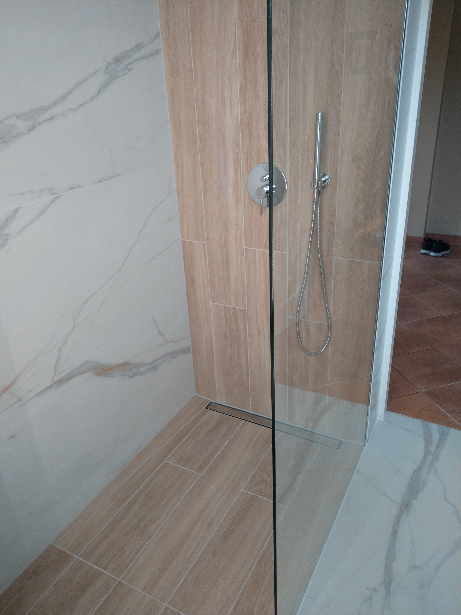 Nowoczesna kabina prysznicowa z odpływem liniowym, wykończona płytkami imitującymi drewno i marmur, widok z boku.