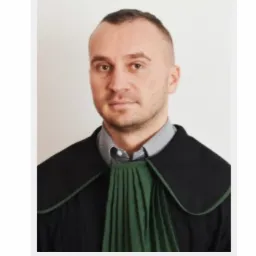 Portret mężczyzny w todze prawniczej z zielonym żabotem na jasnym tle.