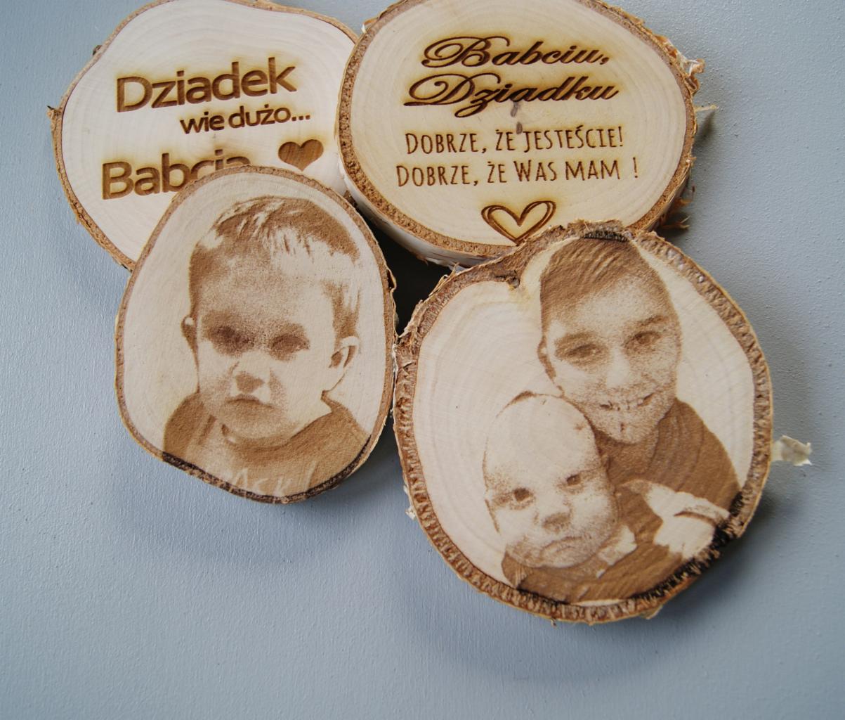 Cztery drewniane plastry z wypalonymi laserowo portretami dzieci i dedykacjami dla dziadków, ułożone na jasnoniebieskim tle.
