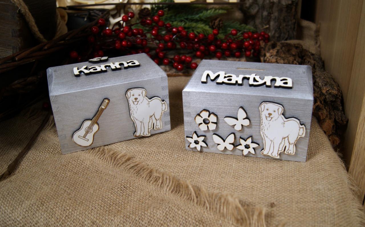 Dwa srebrne, drewniane pudełka z imionami 'Karina' i 'Martyna', ozdobione wycinankami: pies, gitara, kwiaty i motyle, na jutowym tle z dekoracjami z gałązek i czerwonych owoców.