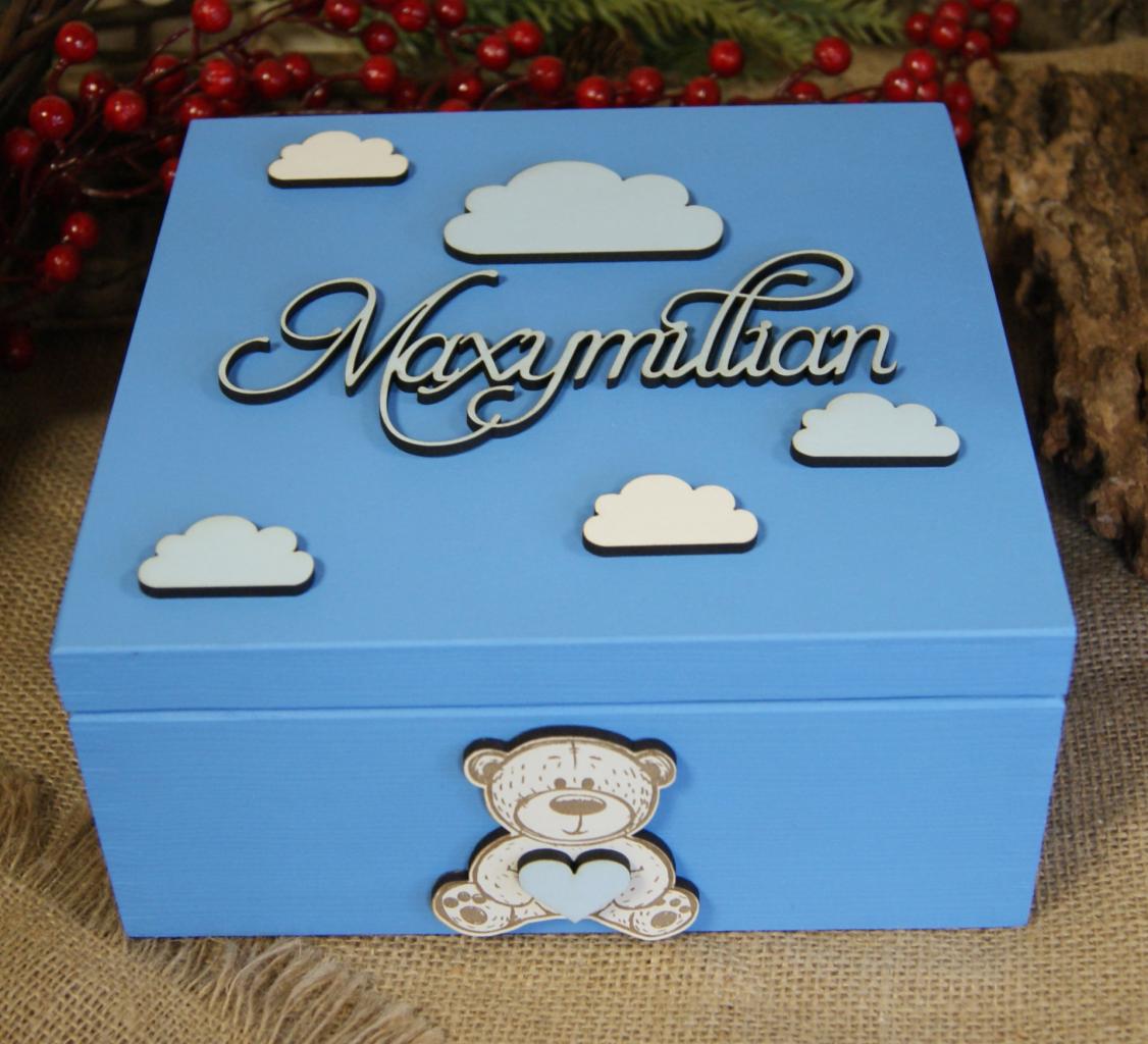 Błękitne, drewniane pudełko z imieniem Maximilian, zdobione chmurkami i misiem trzymającym serce, na tle świątecznych dekoracji.