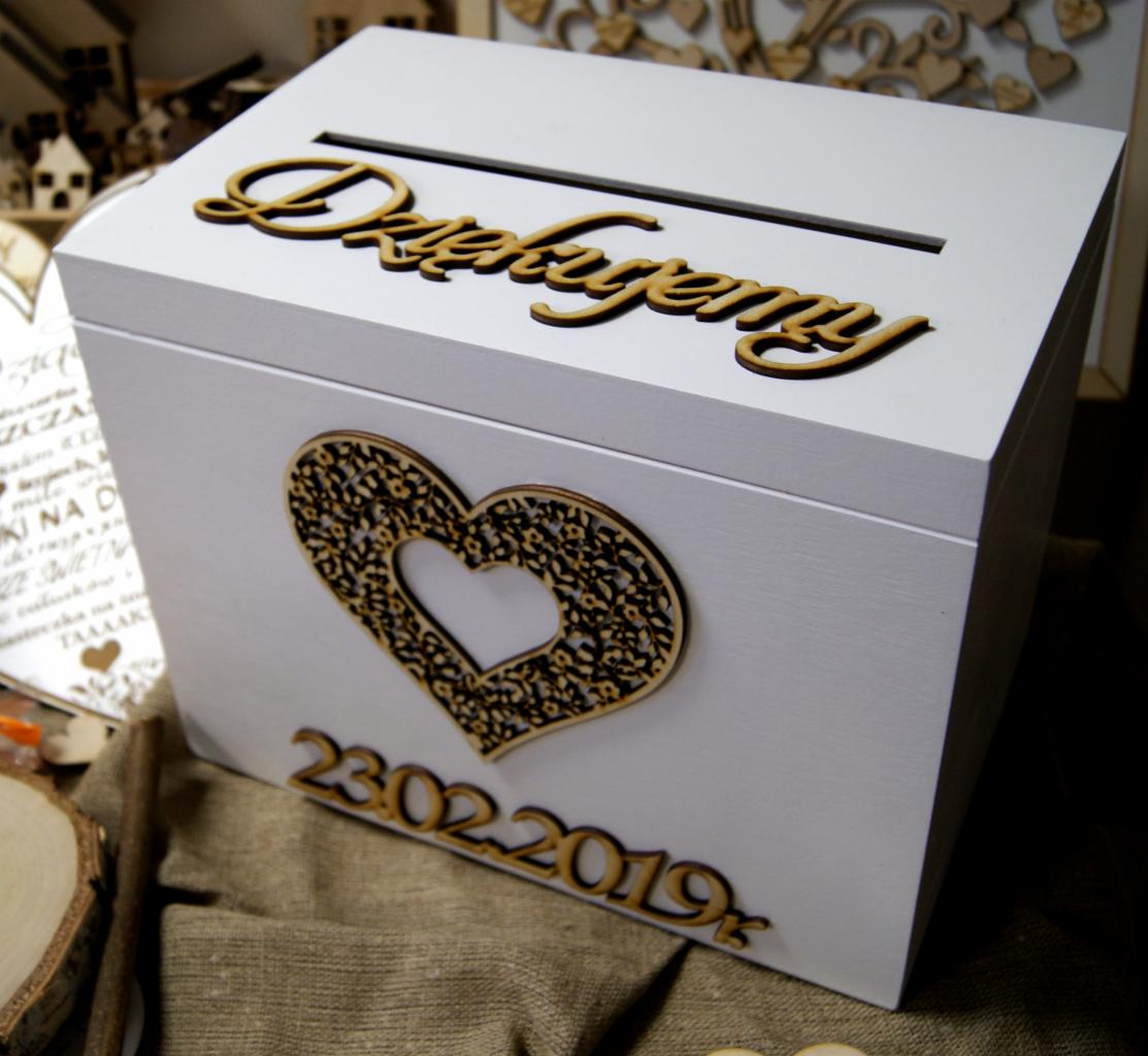 Białe pudełko z napisem 'Dziękujemy', ozdobnym sercem i datą 23.02.2019 wykonane z drewna, z widocznym otworem na koperty, ustawione na jutowym tle.