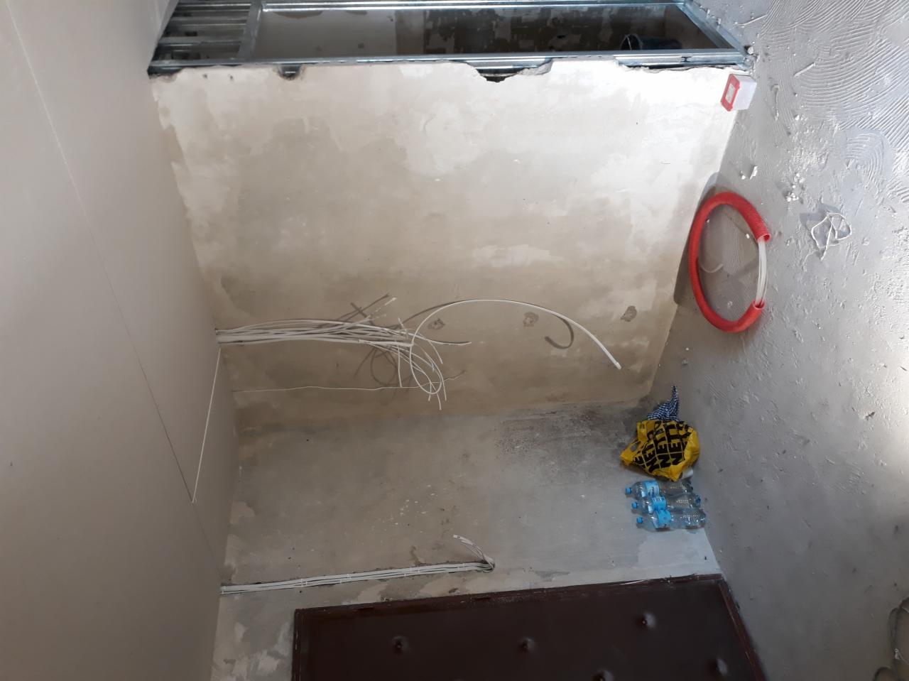 Wiązka białych kabli zwisająca z sufitu w trakcie instalacji, widoczna metalowa konstrukcja sufitu podwieszanego, fragment czerwonej rury karbowanej na ścianie, torba i butelki na podłodze...