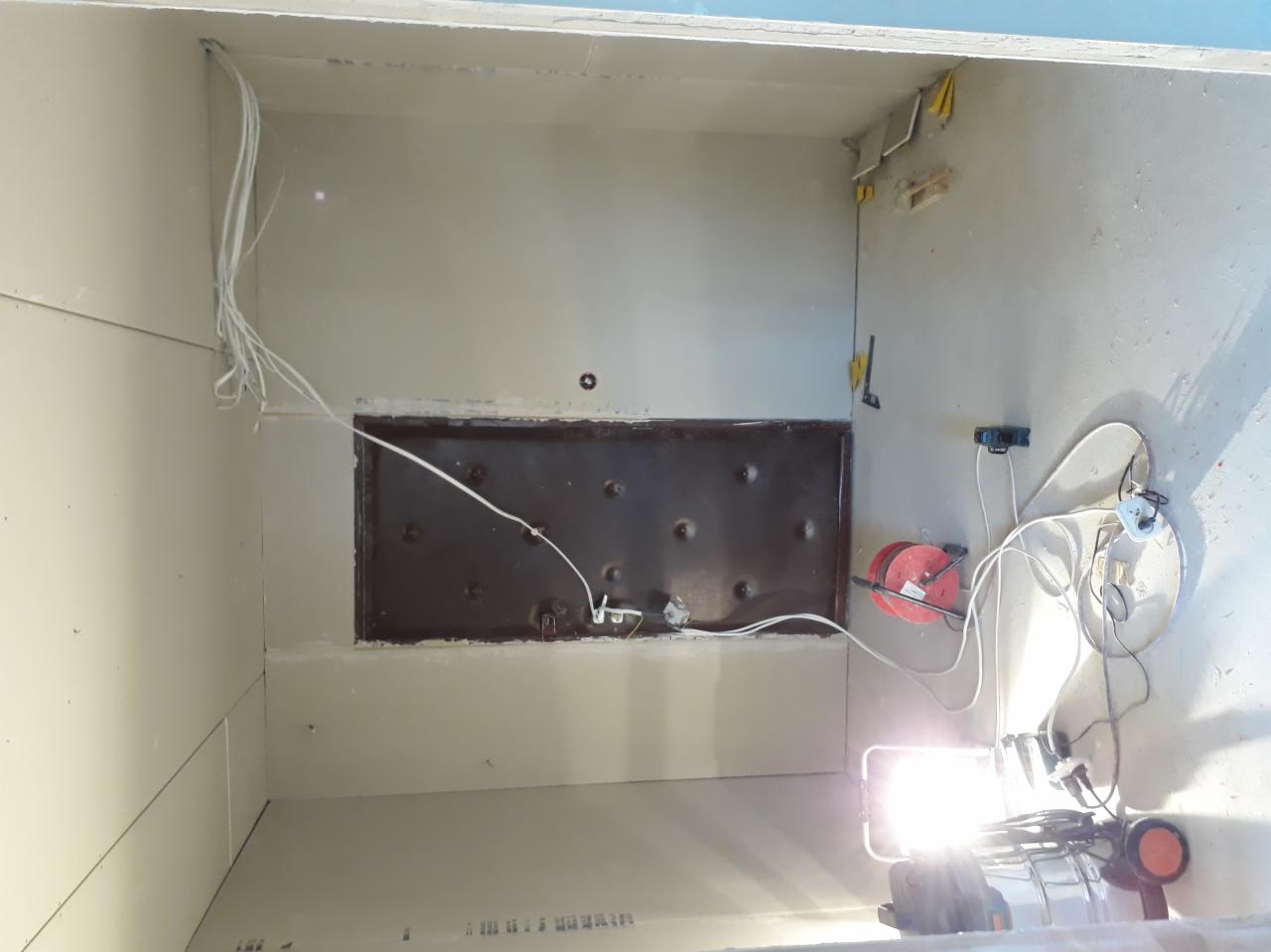 Niedokończona instalacja elektryczna wewnątrz szafy wnękowej: widoczne przewody, puszka instalacyjna, przedłużacz bębnowy i lampa budowlana.