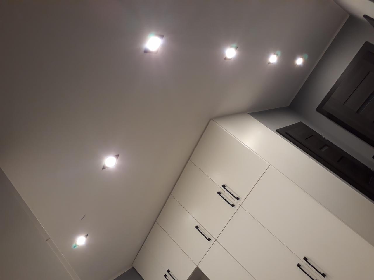 Zamontowane oświetlenie punktowe LED w suficie podwieszanym oraz zabudowa meblowa w Rumi, widok z dołu pod kątem.